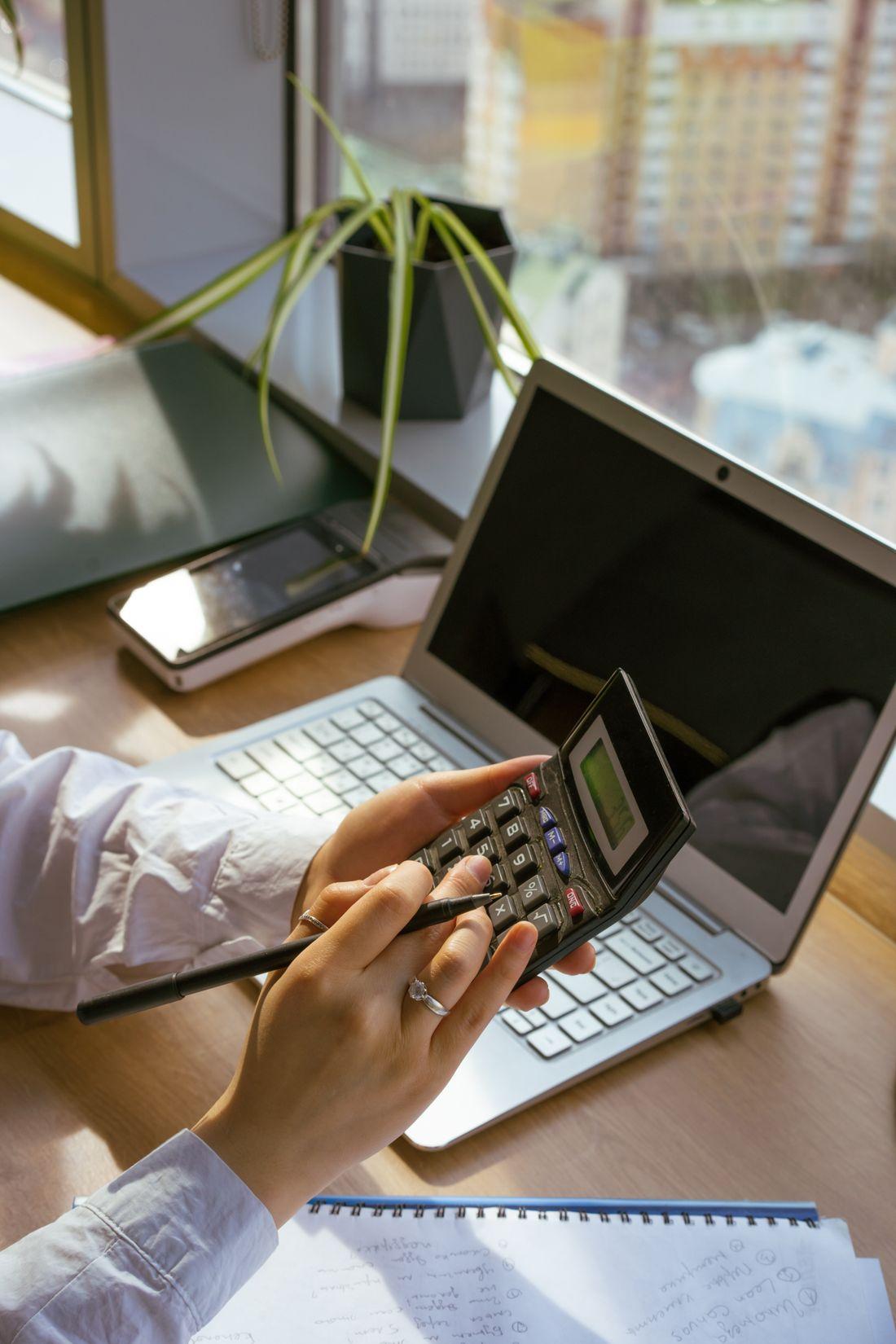 Bàn tay bấm máy tính bên cạnh laptop và cây nhỏ