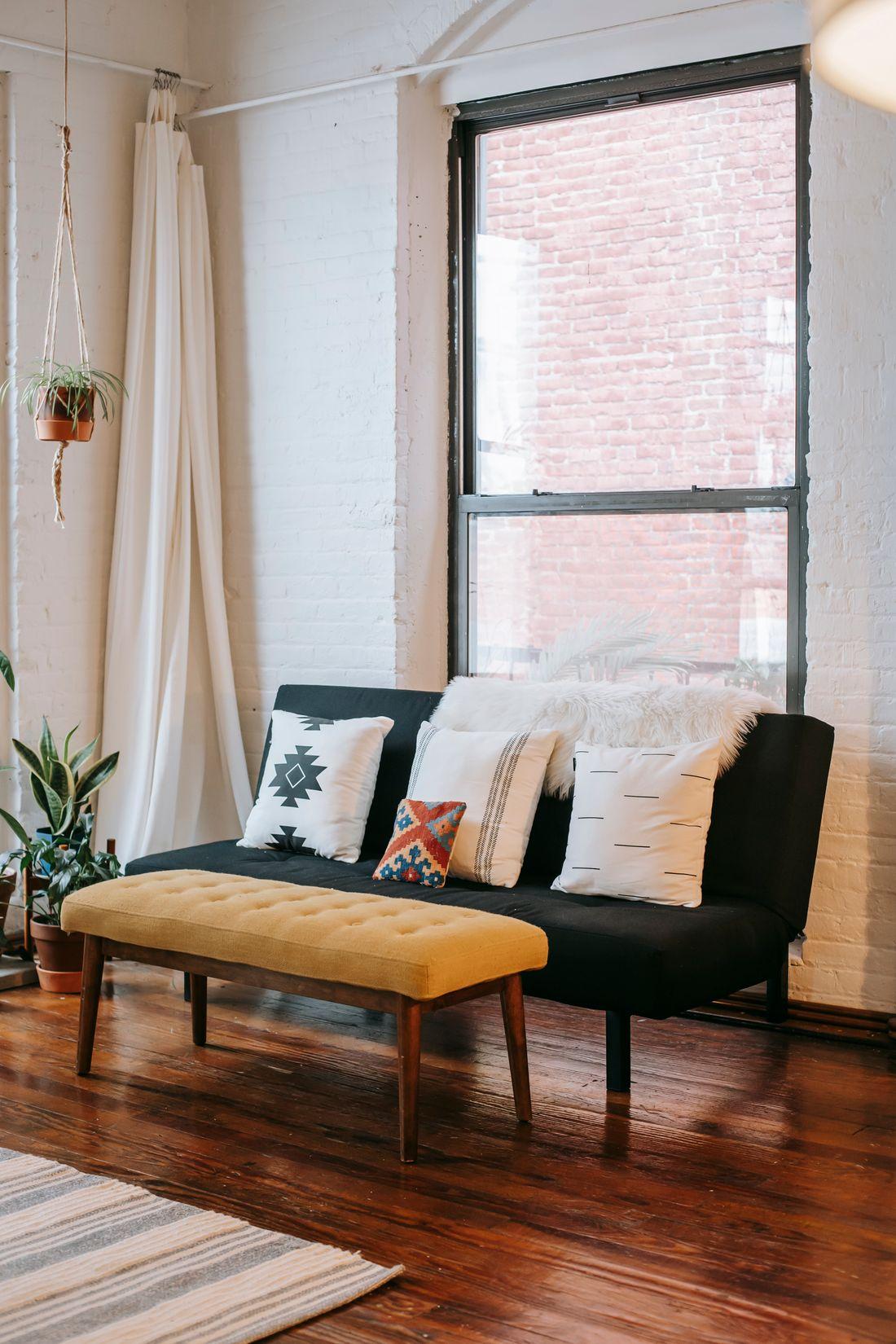 Sofa đen bên cửa sổ gạch, cây xanh trong phòng